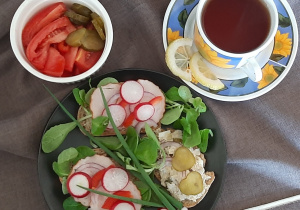 Kolorowe kanapki z rzodkiewką .Obok herbata w kolorowej filiżance i pokrojone warzywa w małym pojemniku.